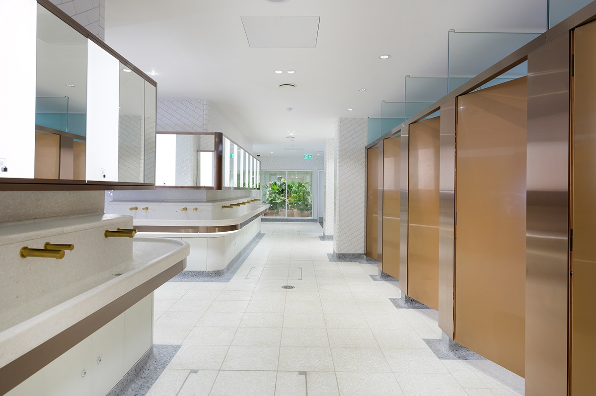 Visual for upgrade of WCs Victoria Station, London showing bronze PVD stainless steel taps and horizontal banding around communal basin. Visual for upgrade of WCs Victoria Station, London showing bronze PVD stainless steel taps and horizontal banding around communal basin.