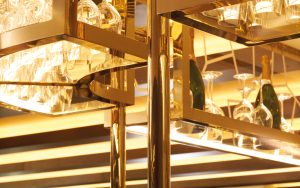 Detail of overhead bar rack in the Brasserie created from V-Grooved Champagne Mirror PVD. The Devonshire Club Hotel - Interior Design: March & White - PVD coloured stainless steel: John Desmond Ltd